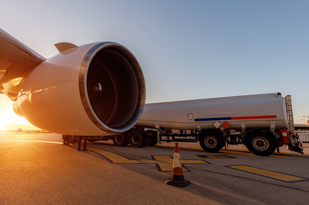 A fuel truck is refueling an aircraft as the sun sets, highlighting the jet engine and operations.